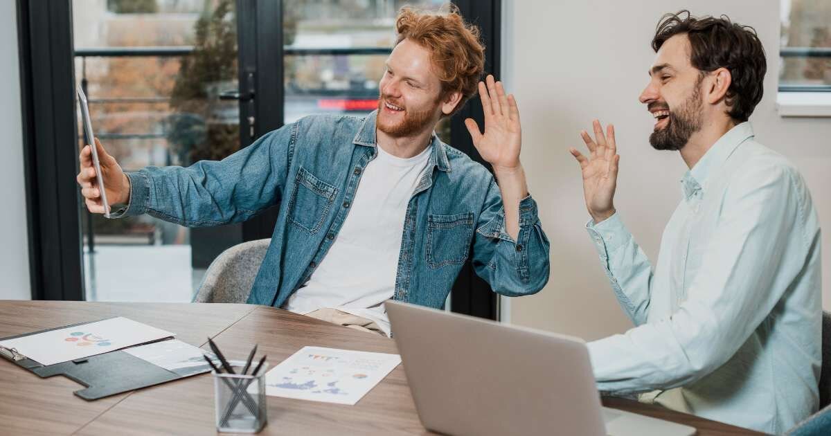 two male colleagues smiling and waving into an ipad 